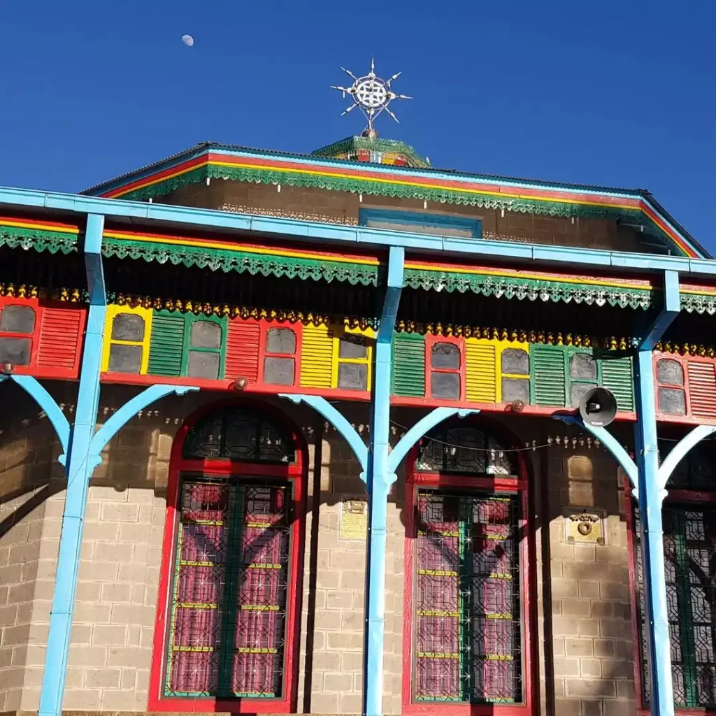 An image of Entoto Maryam Church, a historically significant church located on Entoto Hill in Addis Ababa, Ethiopia. The church's exterior features its characteristic bright colors – red, yellow, green, and blue – adorning its stone and corrugated iron structure. Entoto Maryam is associated with Emperor Menelik II and is a prominent religious and historical site in Addis Ababa.