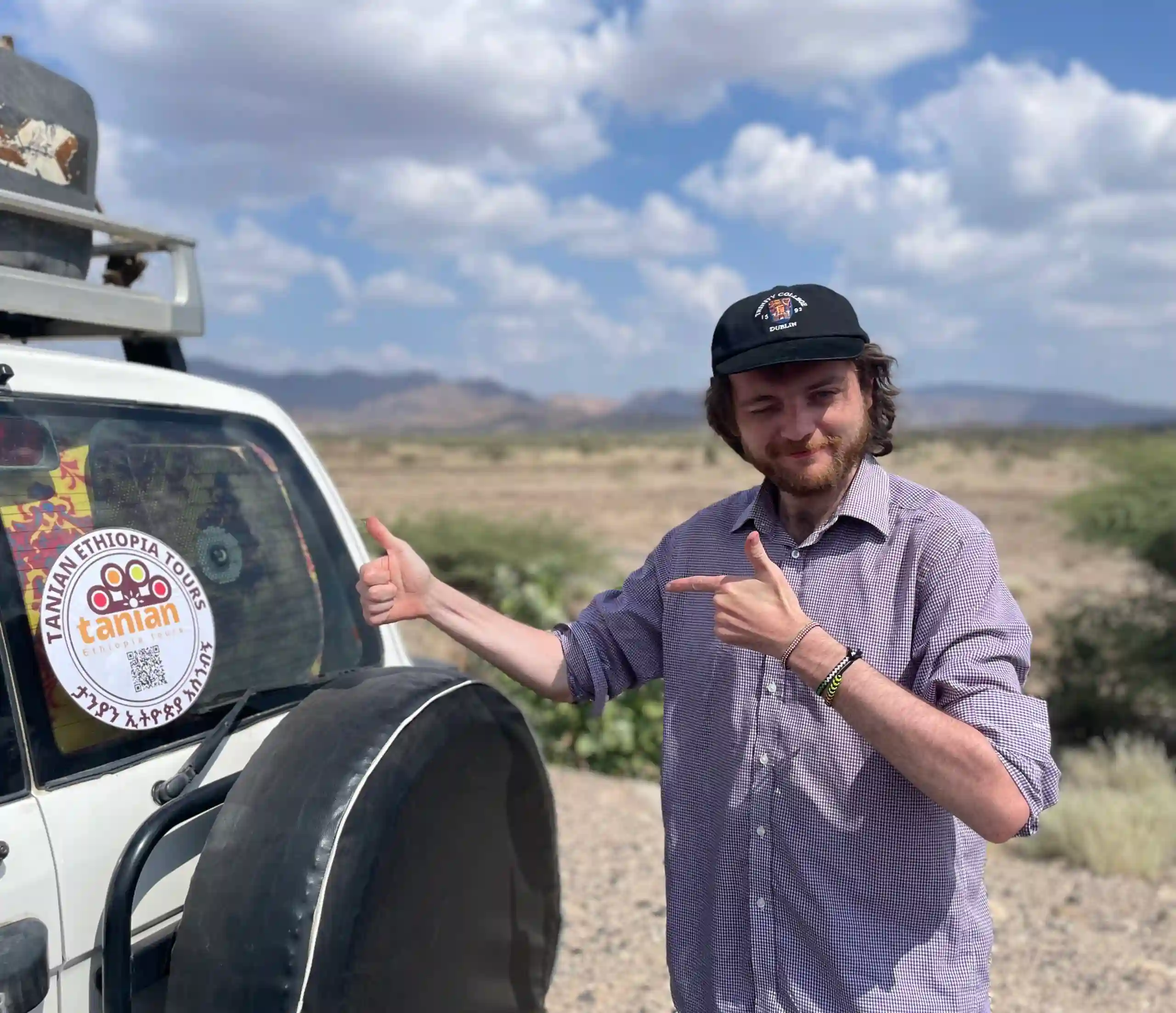 A happy client stands next to Tanian Ethiopia Tours vehicle, displaying the company logo, ready to embark on an exciting Ethiopian adventure.