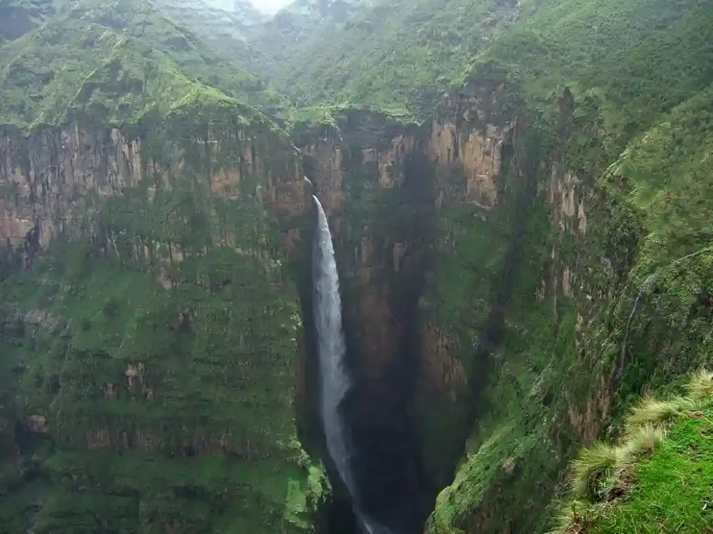 Dramatic view of Jinbar Falls cascading down a steep cliff in Simien Mountains National Park, Ethiopia. The waterfall plunges into a deep gorge surrounded by lush green vegetation on the cliff faces.