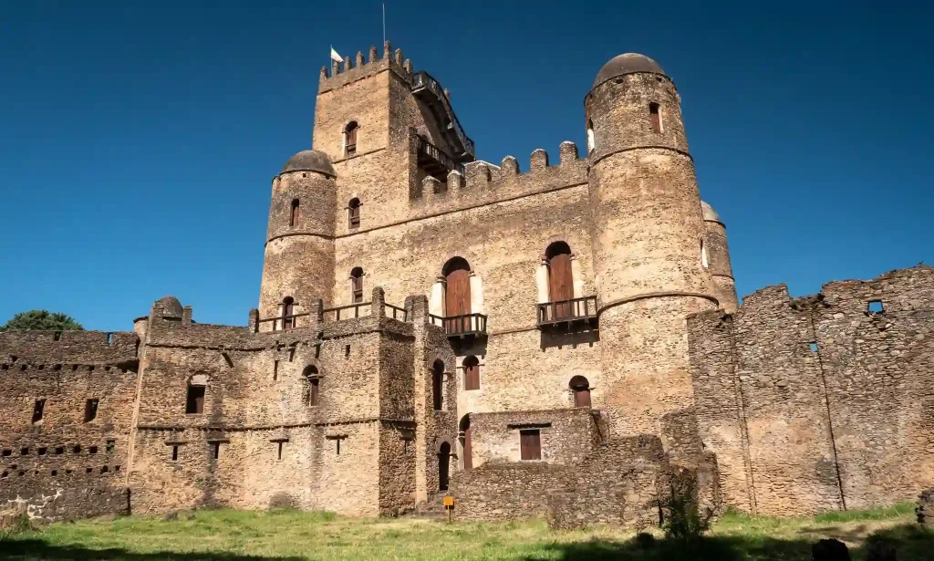 Gonder Castle, a UNESCO World Heritage Site in Ethiopia, featuring multiple stone buildings with crenellations and towers, set against a blue sky.