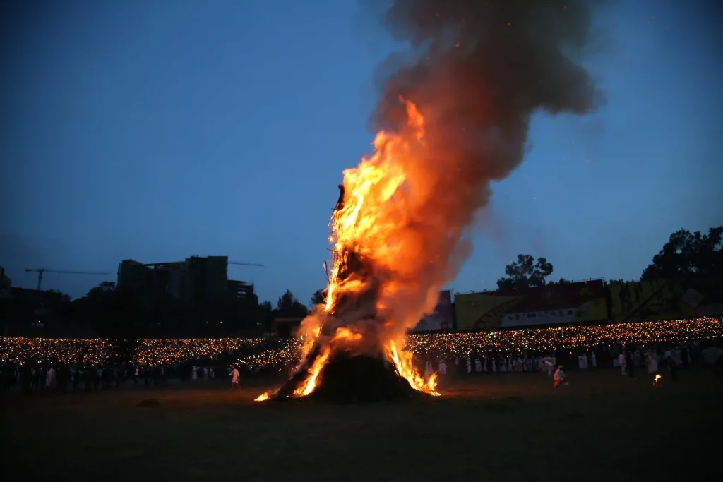 Photograph of the Meskel Festival Demera bonfire burning brightly at night in Ethiopia. A large crowd is gathered around the fire for the celebration.