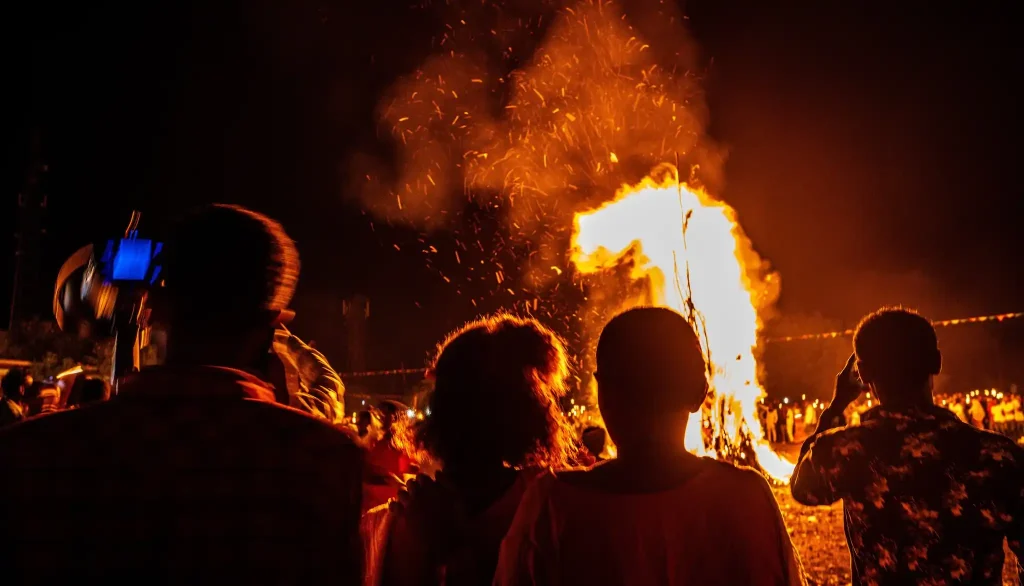 A very large bonfire is burning at night. Many people are standing in a crowd around the fire. This is the Meskel Festival bonfire (Demera) in Ethiopia.