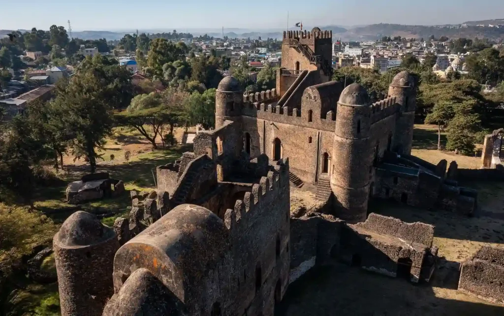 Aerial view of the main entrance and palace buildings within Fasil Ghebbi, the Royal Enclosure in Gondar, Ethiopia. The image shows the stone castle complex with its towers, walls, and courtyards, set against a backdrop of the city and surrounding hills.