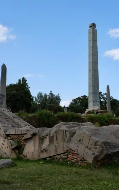 Several monolithic stelae stand in a field at Axum, a UNESCO World Heritage Site, with the modern dome of St. Mary of Zion Church behind.