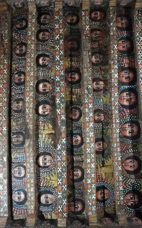 The iconic ceiling of Debre Birhan Selassie Church in Gondar, Ethiopia, adorned with countless painted angle faces, viewed from below.