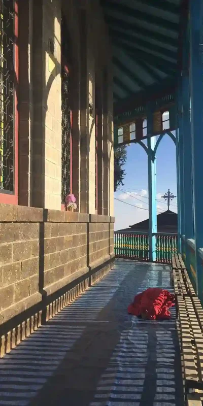 An image of Entoto Maryam Church, a historically significant church located on Entoto Hill in Addis Ababa, Ethiopia. The church's exterior features its characteristic bright colors – red, yellow, green, and blue – adorning its stone and corrugated iron structure. Entoto Maryam is associated with Emperor Menelik II and is a prominent religious and historical site in Addis Ababa.