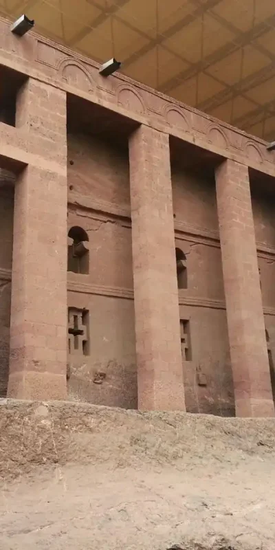 Extrior view of Bete Medhane Alem, a large monolithic rock-hew church in Lalibela. The church is made of reddish-brown rock and has tall, rectangular columns.