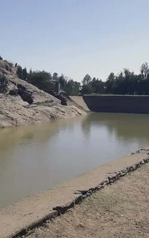 Photograph of Mai Shum, also known as Queen Sheba's Bath, a historical stone-walled reservoir in Axum, Ethiopia. A rocky hillside and steps are visible.