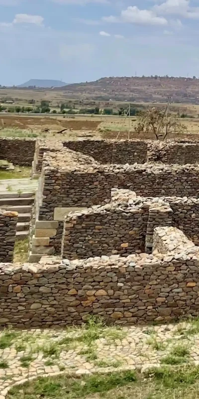 The ruins of Dungur Palace, also known as the Queen of Sheba's Palace, in Aksum, Ethiopia. The image shows weathered stone walls, a paved pathway, and steps leading to different levels of the palace complex.